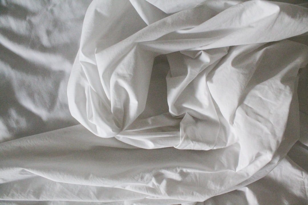 Neatly made bed with crisp white cotton sheets tucked over a tall mattress